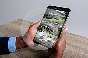 Hands of african american man holding tablet with view of home from security cameras on screen