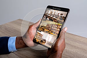 Hands of african american man holding tablet with view of library from security cameras on screen