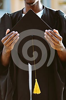 Hands of african american student in black mantle holding graduation hat closeup. Young specialist, graduate from