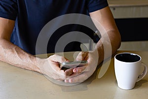 Hands of anonymous man with cellphone on table and coffee cup