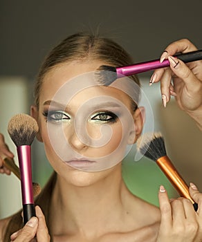 Hands apply makeup on model face. Woman getting powder on skin with brushes, makeup. Woman with young face in beauty