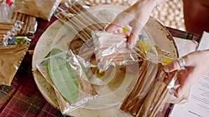 Hands arrange cinnamon sticks and leaf packs on ceramic plate at market stall. Visitor examines, selects aromatic