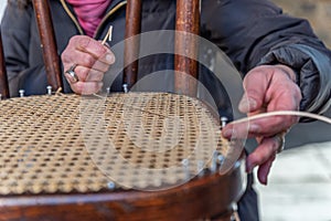 The hands of an artisan weave the wooden chair