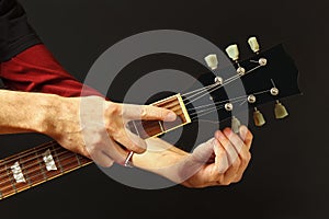 Hands of artist tunes the guitar on dark background