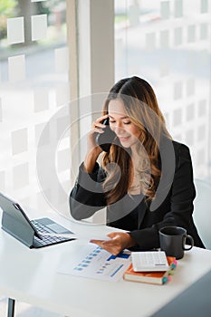 Hands of Asian businesswoman using smartphone and mobile calculator Work on a laptop computer with a calculator on the table with