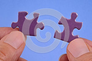 Hands assembling two puzzle pieces close up on blue background