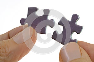 Hands assembling two puzzle pieces close up on white background