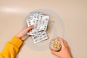 Hands with assorted pharmaceutical medicine pills, tablets and capsules over beige background