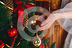 Hands with ball . Young woman decorating Christmas tree with red balls at home