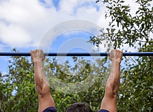 Hands on the bar close-up. The man pulls himself up on the bar. Playing sports in the fresh air. Horizontal bar.