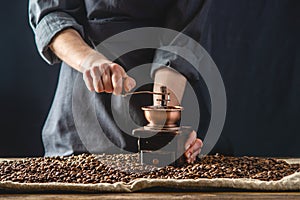 Hands baristas in a dark apron grind on a manual grinder fragrant coffee beans. Selection of fresh coffee for espresso