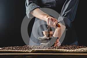 Hands baristas in a dark apron grind on a manual grinder fragrant coffee beans. Selection of fresh coffee for espresso