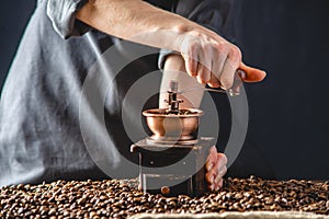 Hands baristas in a dark apron grind on a manual grinder fragrant coffee beans. Selection of fresh coffee for espresso