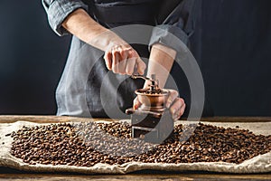 Hands baristas in a dark apron grind on a manual grinder fragrant coffee beans. Selection of fresh coffee for espresso