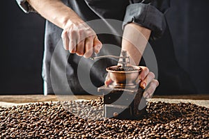 Hands baristas in a dark apron grind on a manual grinder fragrant coffee beans. Selection of fresh coffee for espresso