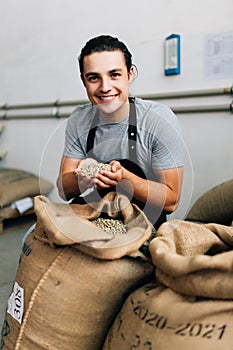 Hands of barrista putting green unroasted coffee beans into sack at factory