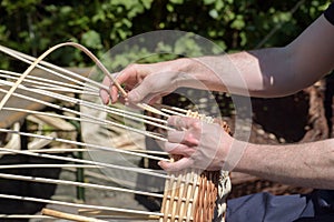 Hands of a basket maker weave a wicker basket