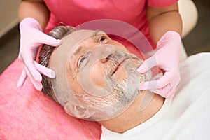 Hands of beautician examining face of man in beautician chair