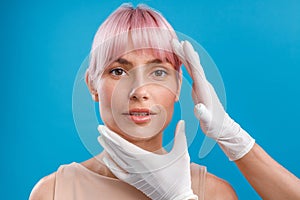 Hands of beautician examining female face before giving facial botox injections isolated over blue background