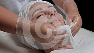 The hands of the beautician wipe the girl`s chin in the cosmetology center with white napkins. Portrait of a beautiful girl on th