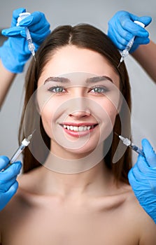 Hands of beauticians holding syringes around flawless woman face ready for injection in cosmetology clinic. Female model