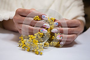 hands with a beautiful multi-colored manicure hold a bouquet of yellow flowers
