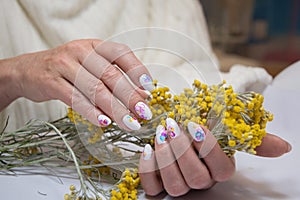 hands with a beautiful multi-colored manicure hold a bouquet of yellow flowers