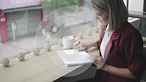 Hands of Beautiful and young successful business woman with book in a cafe, reading the book. Blonde Female in red