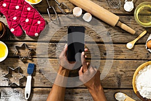 Hands of biracial man holding smartphone by flour, oil, glove, cutters, whisks and rolling pin