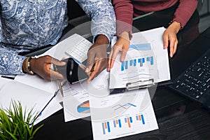 Hands of black people holding mobile phone on background of financial documents in business space close-up