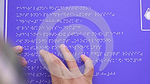 Hands of a blind man in a shirt reading a braille font on a building sign