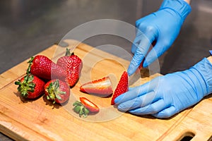 Hands in blue gloves cut red strawberries on a wooden Board for fruit salad.