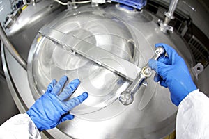 Hands in blue gloves opening industrial process tank