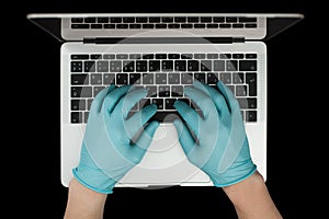 Hands in blue protective gloves typing on laptop keyboard. Top view. Coronavirus concept