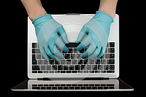 Hands in blue protective gloves typing on laptop keyboard. Top view. Coronavirus concept