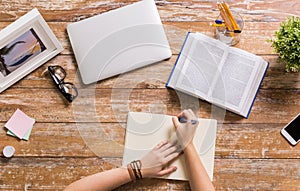 Hands with book writing to notebook at table