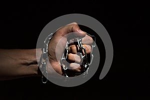 Hands bound in metal chains on a black background