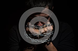 Hands bound in metal chains on a black background