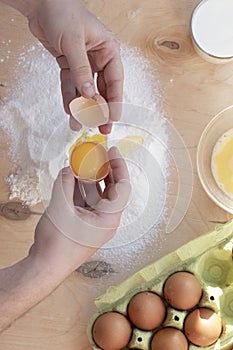 Hands break a raw egg. Stir the protein with the yolk. Sifting flour through a sieve on a wooden background. Glass bowl with mix
