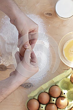 Hands break a raw egg. Stir the protein with the yolk. Sifting flour through a sieve on a wooden background. Glass bowl with mix