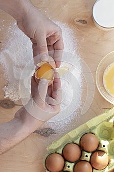 Hands break a raw egg. Stir the protein with the yolk. Sifting flour through a sieve on a wooden background. Glass bowl with mix