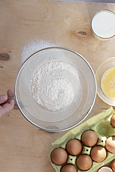 Hands break a raw egg. Stir the protein with the yolk. Sifting flour through a sieve on a wooden background. Glass bowl with mix