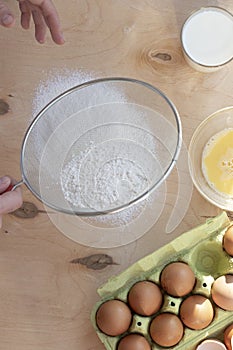 Hands break a raw egg. Stir the protein with the yolk. Sifting flour through a sieve on a wooden background. Glass bowl with mix