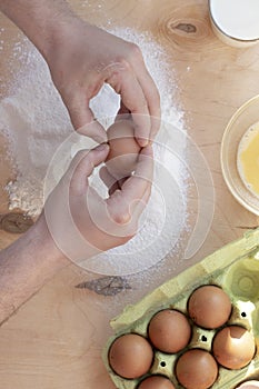 Hands break a raw egg. Stir the protein with the yolk. Sifting flour through a sieve on a wooden background. Glass bowl with mix