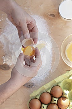 Hands break a raw egg. Stir the protein with the yolk. Sifting flour through a sieve on a wooden background. Glass bowl with mix