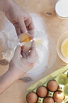 Hands break a raw egg. Stir the protein with the yolk. Sifting flour through a sieve on a wooden background. Glass bowl with mix