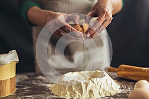 Woman hands breaking egg into raw dough on wooden table