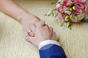 hands of a bride and a bridegroom, just married, a bridal bouquet is beside