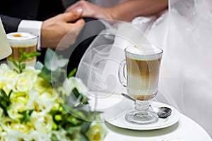 Hands of the bride and groom for a cup of coffee. Wedding bouquet on the table.