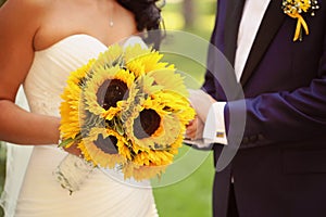 Hands of a bride and groom holding sunflower bouquet
